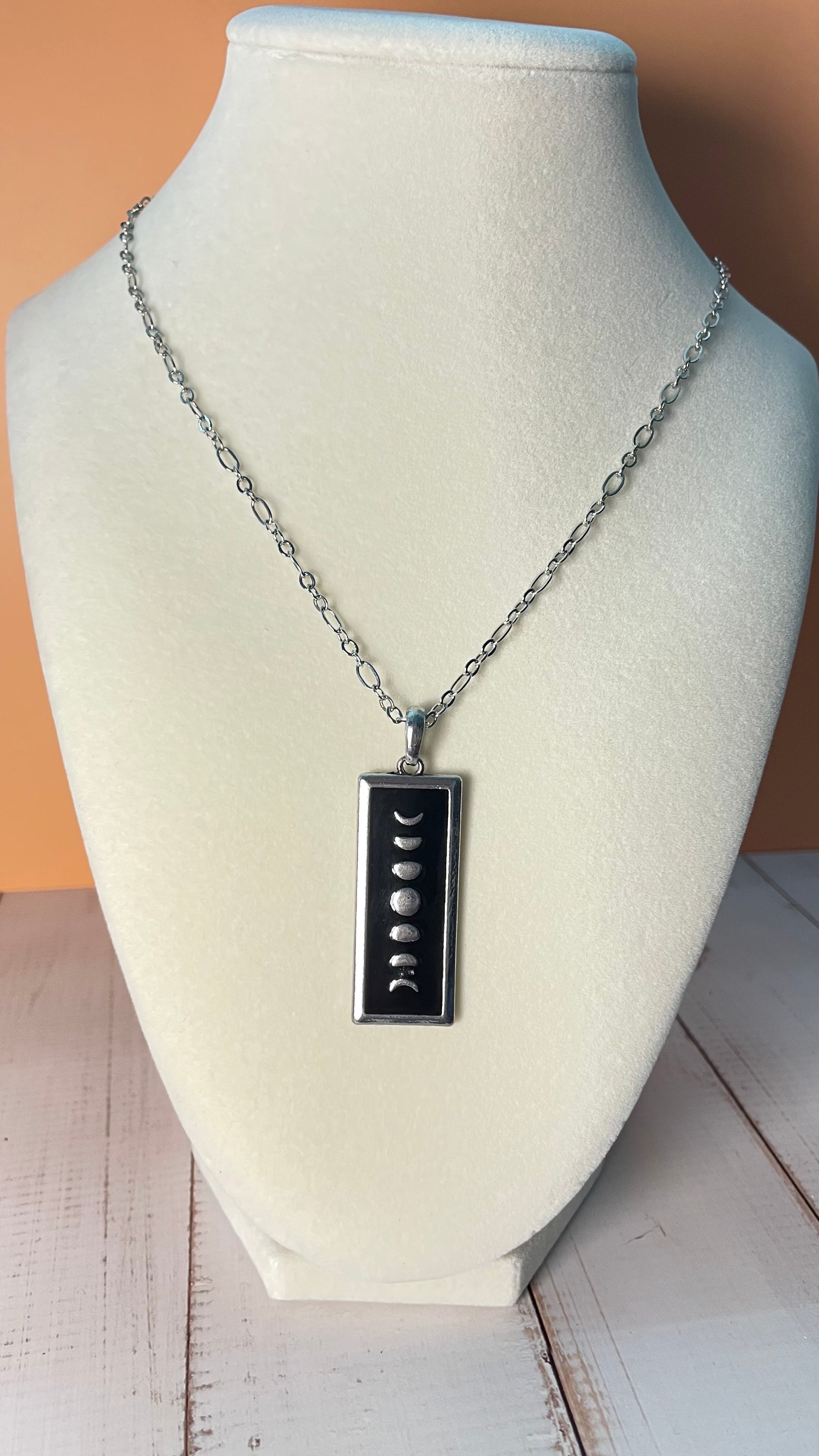 Black and silver moon phase pendant on a silver chain displayed on a mannequin bust